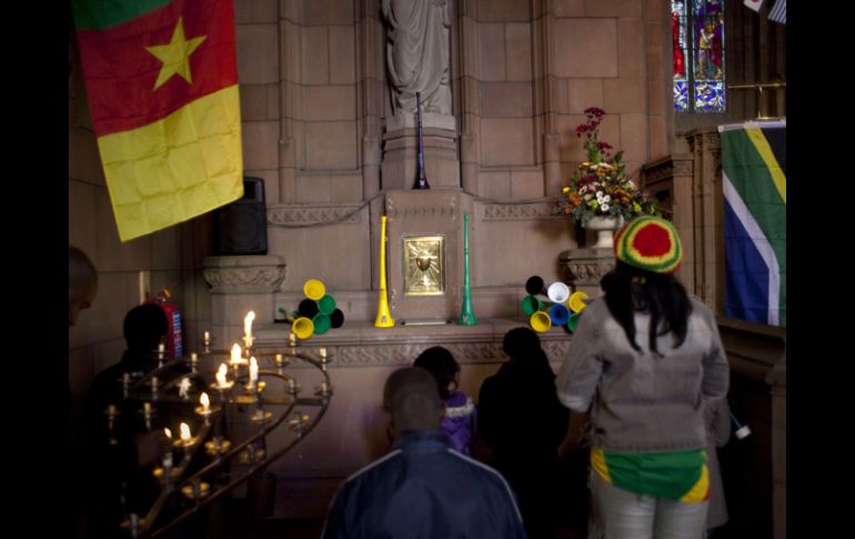 Aficionados sudafricanos oran a una figura de Jesucristo adornada con vuvuzelas y banderas en la Catedral de Pretoria. AP  /