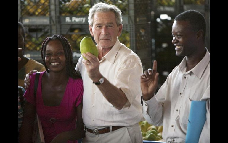 El ex presidente George W. Bush muestra un mango, acompañado del dueño de la empresa Ralph Perry, y de unas trabajadoras. EFE  /