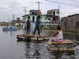 Personas cruzan las calles en albercas de fibra de vidrio y objetos habilitados como balsas provisionales por inundaciones. REUTERS  /