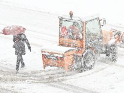 Un peatón camina bajo una fuerte nevada junto a una excavadora que intenta despejar las calles de nieve en St. Gallen (Suiza). EFE  /