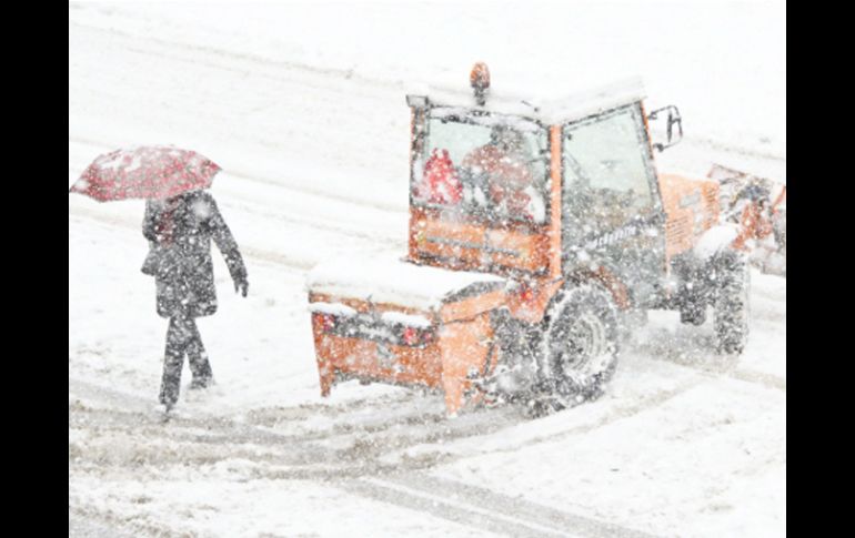 Un peatón camina bajo una fuerte nevada junto a una excavadora que intenta despejar las calles de nieve en St. Gallen (Suiza). EFE  /