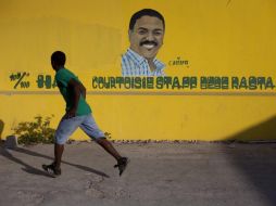 Un hombre corre frente a un muro pintado con la figura del candidato presidencial Jude Celestin. EFE  /