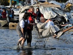 Un par de ciudadanos transportan a un anciano por una avenida de la localidad de Ishinomaki, Miyagi, afectada por el sismo. EFE  /