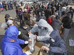 Evacuados forman fila para recibir raciones de arroz y otros alimentos, en el centro de distribución de Minamisoma. AP  /