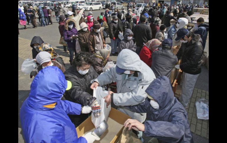 Evacuados forman fila para recibir raciones de arroz y otros alimentos, en el centro de distribución de Minamisoma. AP  /