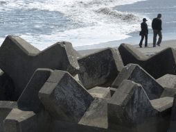 Una pareja pasea por la playa, en la que quedaron semienterrados bloques gigantes de cemento de un rompeolas tras el tsunami. EFE  /