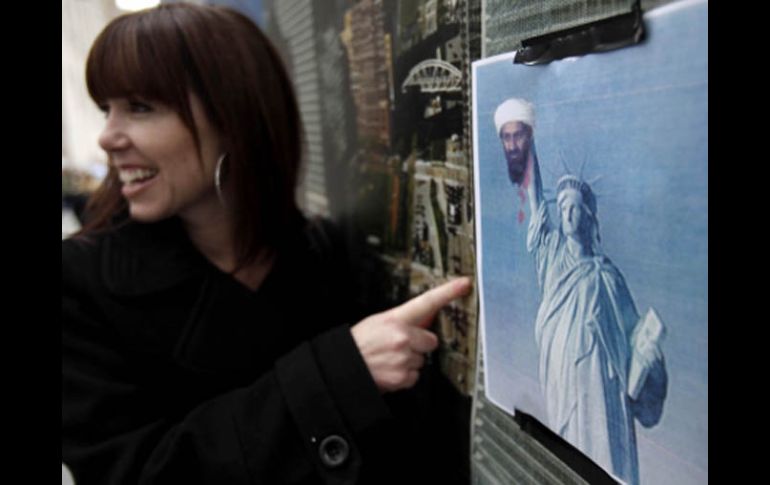 Una turista posa junto a un cartel donde se muestra a la estatua de la libertad sosteniendo la cabeza del Osama Bin Laden. AP  /