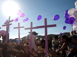 Personas ponen globos frente a cruces de tumbas durante el paso de la caravana contra la violencia. AFP  /