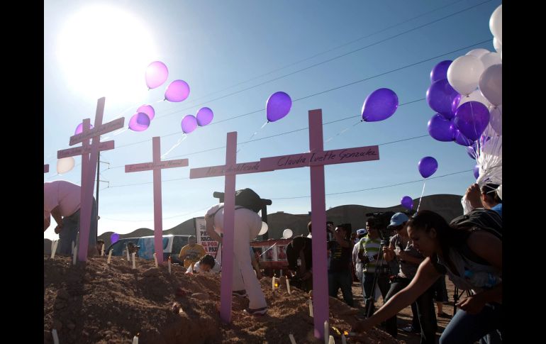 Personas ponen globos frente a cruces de tumbas durante el paso de la caravana contra la violencia. AFP  /