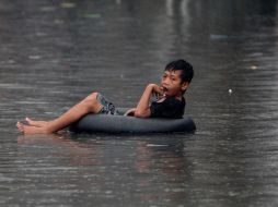 Un niño flota en las aguas de la inundación montado en un neumático, en Quezon City, Manila. EFE  /