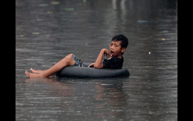 Un niño flota en las aguas de la inundación montado en un neumático, en Quezon City, Manila. EFE  /