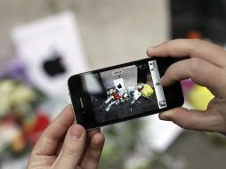 Un hombre toma con un iPhone una foto de flores en memoria de Jobs afuera de una sucursal de Apple en París. AFP  /