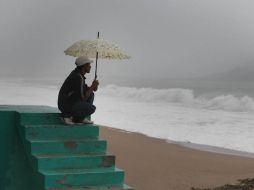 Un habitante de Melaque, en Jalisco, observa hoy el mar agitado mientras se cubre de la lluvia.  /