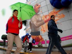 Una mujer se protege de la lluvia mientras camina frente a promocionales de los Juegos. EFE  /