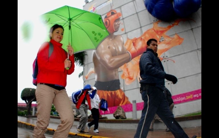 Una mujer se protege de la lluvia mientras camina frente a promocionales de los Juegos. EFE  /