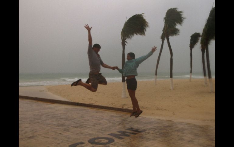 Unos turistas saltan en la playa mientras las lluvias de ''Rina'' aún se dejaban sentir. AP  /