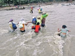 Filipinos cargan con las pocas pertenencias que les quedan mientras luchan contra la corriente para poder atravesar un río. EFE  /