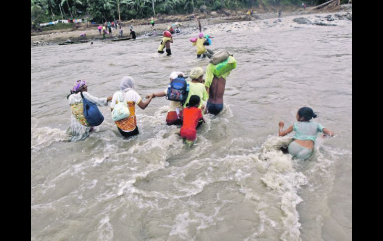 Filipinos cargan con las pocas pertenencias que les quedan mientras luchan contra la corriente para poder atravesar un río. EFE  /