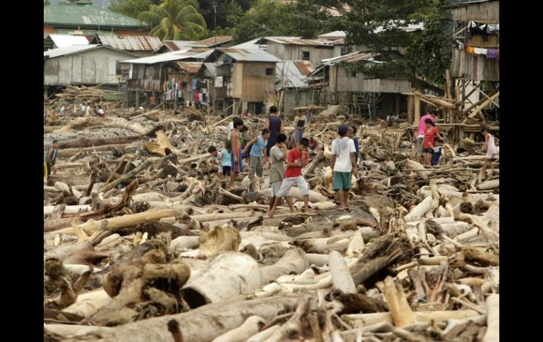 Varios damnificados por las inundaciones caminan entre troncos arrastrados por las aguas. EFE  /