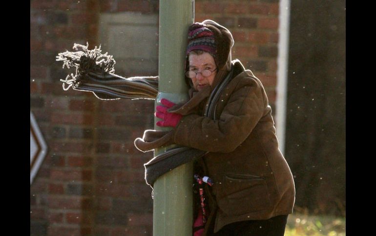 Una mujer tiene que sostenerse de un poste debido a los fuertes vientos en Inglaterra. AP  /