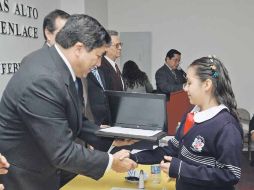 Antonio Gloria Morales entrega una computadora a una de las estudiantes destacadas de la prueba ENLACE.  /