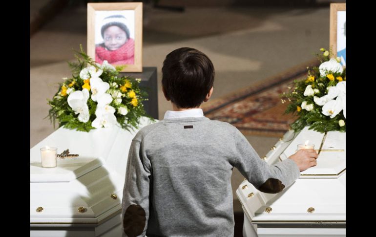 Un niño deja una vela en un ataúd durante el funeral de seis de los niños. EFE  /