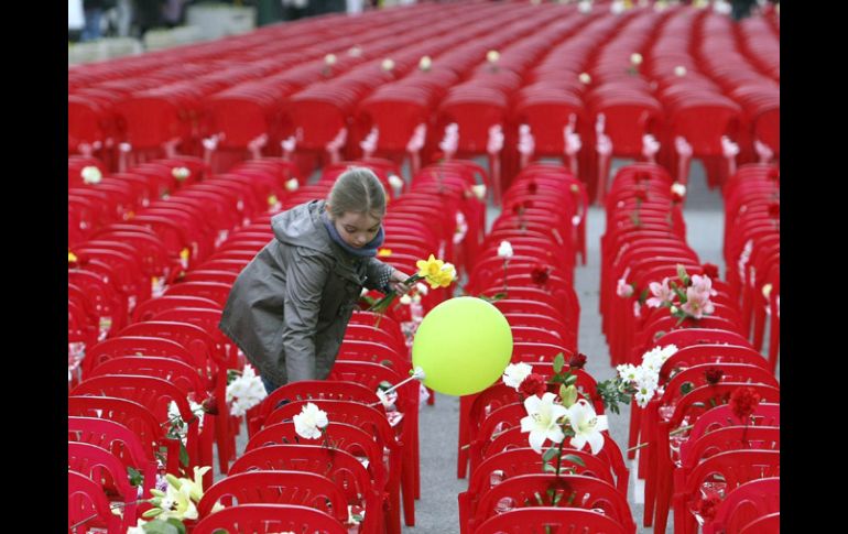 Una niña deja flores sobre algunas de las 11 mil 541 sillas rojas que ocupan la calle principal de Sarajevo. EFE  /