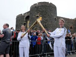 Kathleen Irvine (i) pasa a Lisa Hickson (d) la llama olímpica fuera de Castillo de Carrickfergus de Irlanda del Norte. AP  /