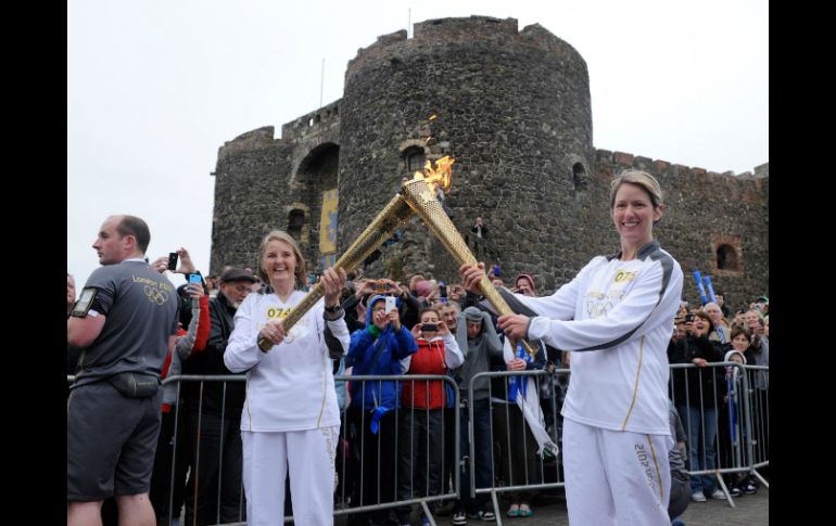 Kathleen Irvine (i) pasa a Lisa Hickson (d) la llama olímpica fuera de Castillo de Carrickfergus de Irlanda del Norte. AP  /