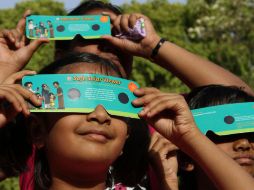 Niñas observan con aditamentos adecuados un eclipse de sol, ilustrando cómo proteger la vista para observar este fenómeno. AP  /