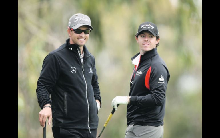 Rory McIlroy (der.), el campeón defensor, charla con el australiano Adam Scott.  /