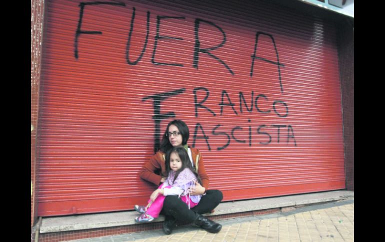 Una mujer y una niña permanecen sentadas al pie de una cortina con una leyenda en repudio al  presidente Federico Franco. REUTERS  /