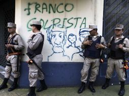 Lo policías paraguayos vigilan las calles, están parados frente a un muro con pintas de los inconformes tras la destitución de Lugo. AP  /