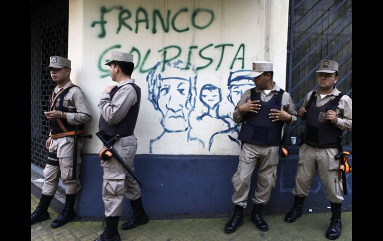 Lo policías paraguayos vigilan las calles, están parados frente a un muro con pintas de los inconformes tras la destitución de Lugo. AP  /