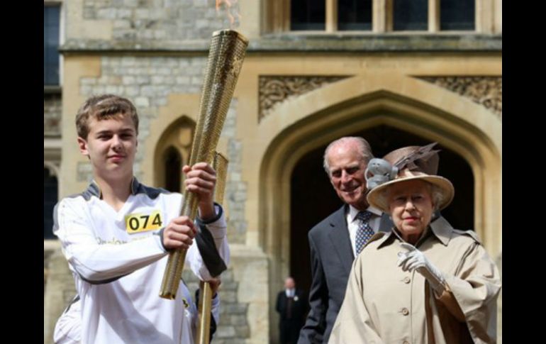 Reina Isabel II y el duque de Edimburgo observar como el atleta Phillip Wells sostiene la llama olímpica. ESPECIAL  /