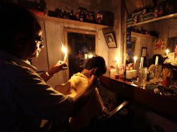 Un hombre realiza un corte de cabello en su peluquería, se apoya con la luz de una vela. AP  /