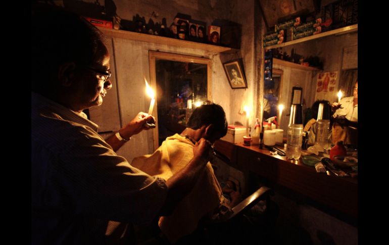 Un hombre realiza un corte de cabello en su peluquería, se apoya con la luz de una vela. AP  /