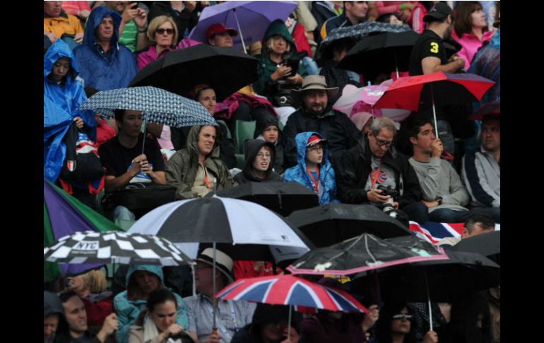 La gente espera la reanudación del partido, cubriéndose de la lluvia. AFP  /