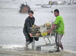 Vendedores de coco recuperan la mercancía después de ser sorprendidos cuando altas olas arrastraron sus palapas. AP  /