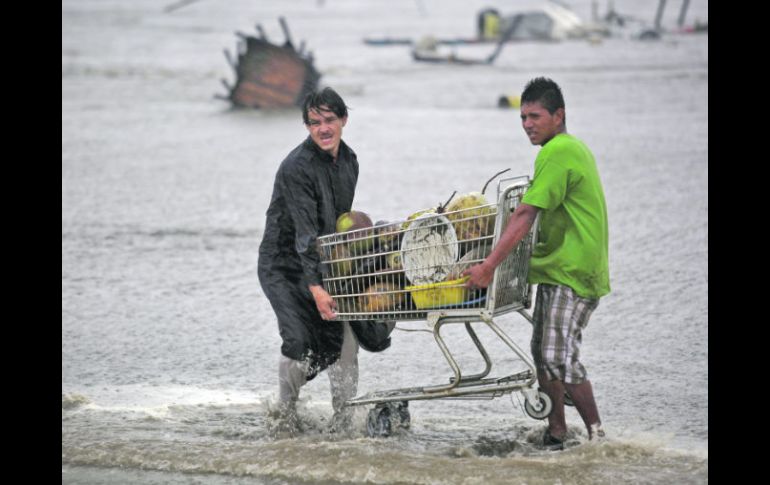 Vendedores de coco recuperan la mercancía después de ser sorprendidos cuando altas olas arrastraron sus palapas. AP  /