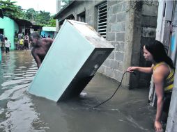 A RESGUARDO. Personas afectadas por una inundación en La Barquita, municipio de Santo Domingo Este, rescatan algunos bienes. EFE  /