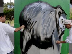 Dos artistas trabajan en una de la columnas que soportan un tramo elevado de la vía del metro en Medellín, Colombia. EFE  /