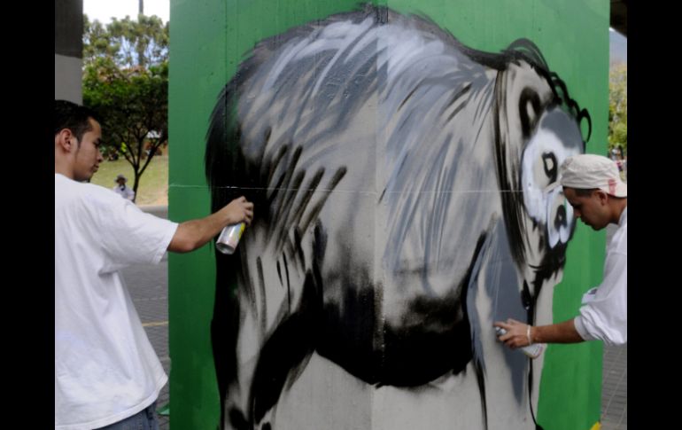 Dos artistas trabajan en una de la columnas que soportan un tramo elevado de la vía del metro en Medellín, Colombia. EFE  /