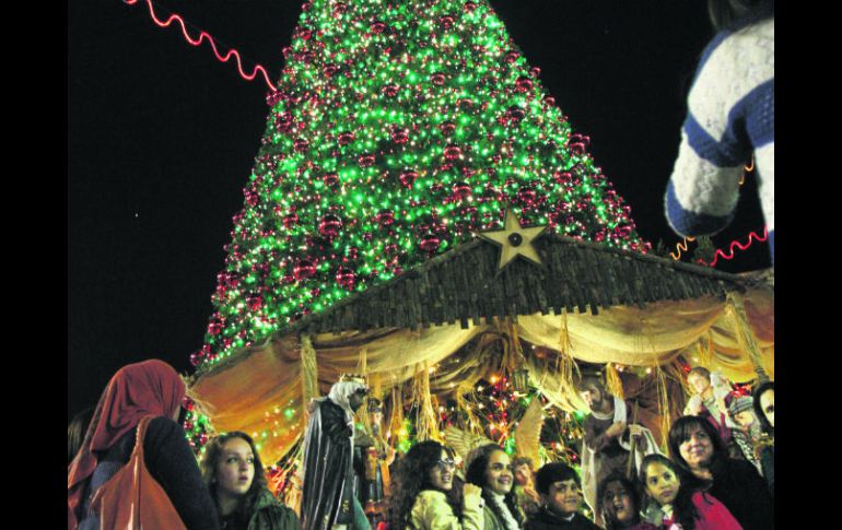 Palestinos posan junto a un árbol de Navidad en el Cuadrado del Pesebre, fuera de la Iglesia de la Natividad, en Belén. AP  /