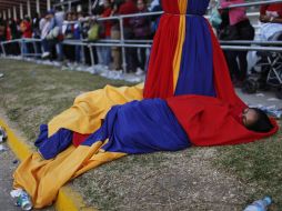 Una mujer duerme en telas con los colores de la bandera, espera que llegue su turno para ver al fallecido mandatario. AP /