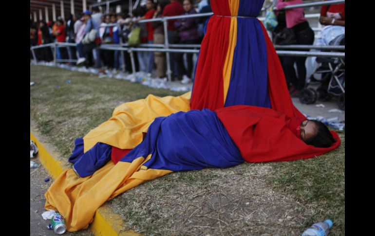 Una mujer duerme en telas con los colores de la bandera, espera que llegue su turno para ver al fallecido mandatario. AP /