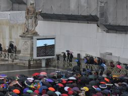 Fieles en la plaza de San Pedro se protegen de la lluvia en espera de ver la ''fumata que indique el resultado de la segunda elección. AFP /