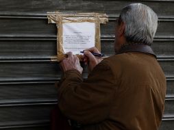 Un hombre escribe la palabra ''deshonra'' en la puerta de la sucursal de un banco chipriota en Atenas. EFE /