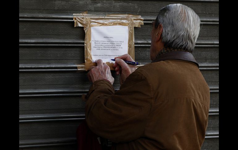 Un hombre escribe la palabra ''deshonra'' en la puerta de la sucursal de un banco chipriota en Atenas. EFE /