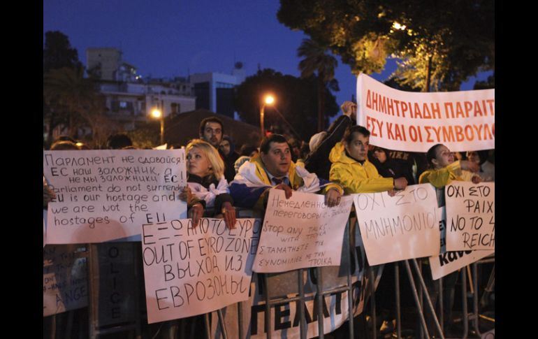 Varios asistentes muestran pancartas durante una manifestación frente al Parlamento de Chipre. EFE /